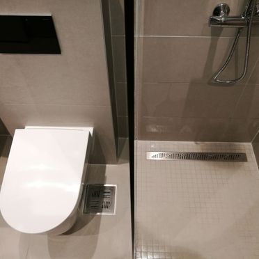 Dusj med mosaikkflis på gulv og rektangulært sluk og toalett avbildet ovenfra