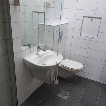 Baderom med rektangulære fliser i hvitt på vegg og grått på gulv, samt vask og toalett
