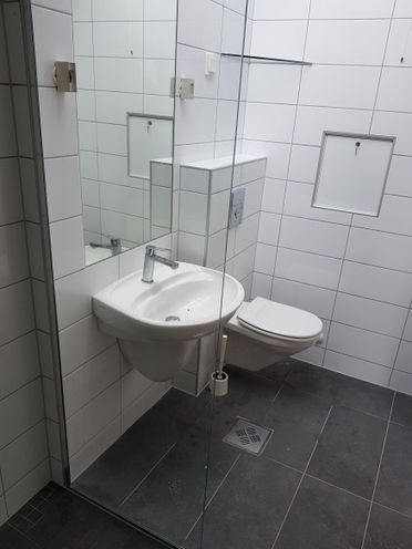 Baderom med rektangulære fliser i hvitt på vegg og grått på gulv, samt vask og toalett