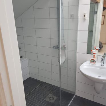 Baderom med hvite fliser på vegg og grå mosaikkfliser på gulv i dusjsone