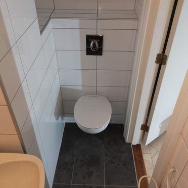 Lite toalett renovert med hvite fliser på vegg og grått gulv