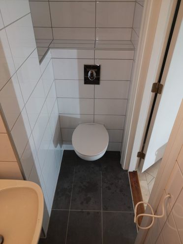 Lite toalett renovert med hvite fliser på vegg og grått gulv
