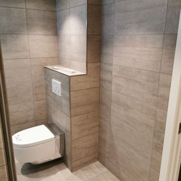 Renovert baderom med grå flis og vegghengt toalett