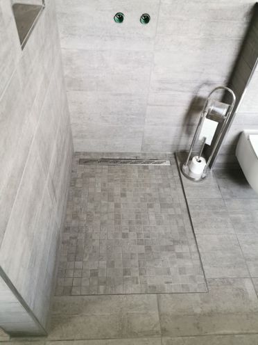 Dusjsone med betong mosaikkflis på gulv og større flis på vegg