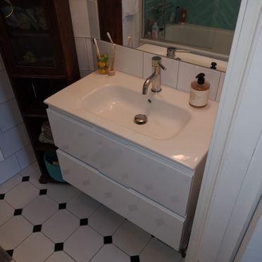 Hvit vaskeservant med skuffer, baderomsspeil og fliskledd gulv