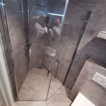 Dusjhjørne på renovert bad med glassdører og flis på vegger og gulv