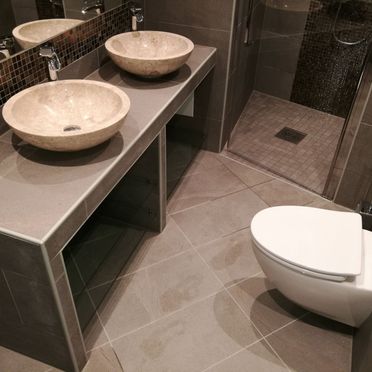 Renovert bad med innebygd vask med oppbevaringsplass og to servanter og vegghengt toalett