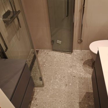 Dusjhjørne i renovert baderom med glassvegger og terrassoflis på gulv