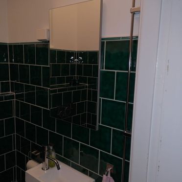 Lite baderom med smaragdgrønne veggfliser og liten servant med speil