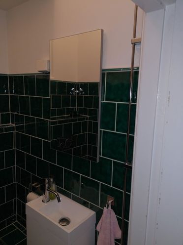 Lite baderom med smaragdgrønne veggfliser og liten servant med speil