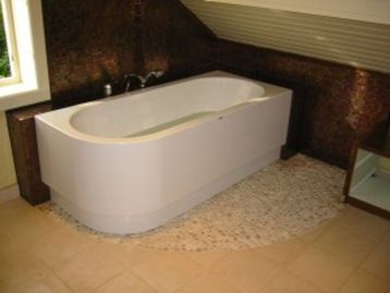  badekar i hjørne av baderom med skråtak med mosaikkflis på gulv og vegg