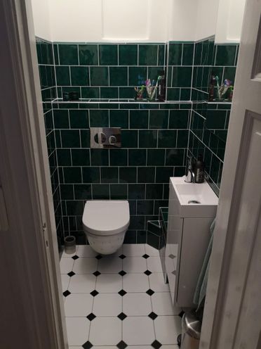 Toalett med smaragdgrønne veggfliser og liten servant