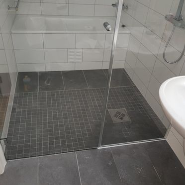 Dusjsone med badekar med små mosaikkfliser i grått på gulv