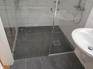 Dusjsone med badekar med små mosaikkfliser i grått på gulv