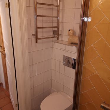 Gammelt baderom med vegghengt toalett og gule fliser på vegg