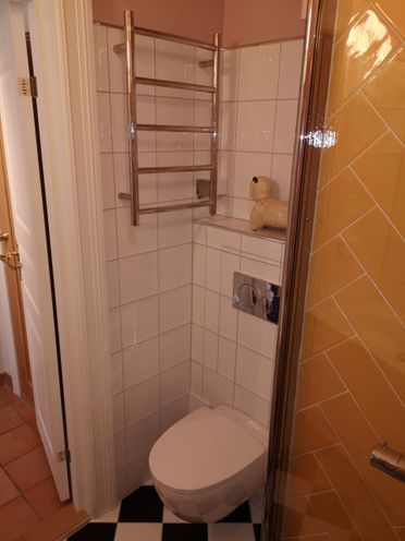Gammelt baderom med vegghengt toalett og gule fliser på vegg