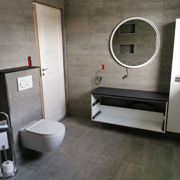 Industrielt bad med vegghengt toalett, hvitt interiør og betongflis